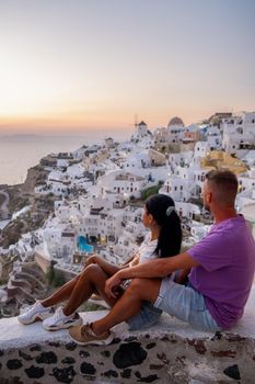 Santorini Greece, young couple on luxury vacation at the Island of Santorini watching sunrise by the blue dome church and whitewashed village of Oia Santorini Greece during sunrise during summer vacation, men and woman on holiday in Greece