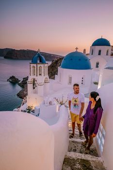 Santorini Greece, young couple on luxury vacation at the Island of Santorini watching sunrise by the blue dome church and whitewashed village of Oia Santorini Greece during sunrise during summer vacation