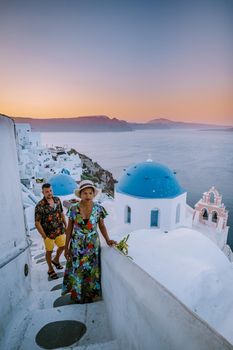 Santorini Greece, young couple on luxury vacation at the Island of Santorini watching sunrise by the blue dome church and whitewashed village of Oia Santorini Greece during sunrise during summer vacation, men and woman on holiday in Greece