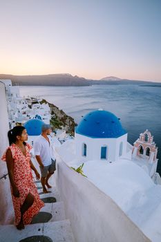 Santorini Greece, young couple on luxury vacation at the Island of Santorini watching sunrise by the blue dome church and whitewashed village of Oia Santorini Greece during sunrise during summer vacation, men and woman on holiday in Greece