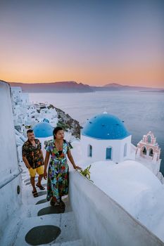 Santorini Greece, young couple on luxury vacation at the Island of Santorini watching sunrise by the blue dome church and whitewashed village of Oia Santorini Greece during sunrise during summer vacation, men and woman on holiday in Greece