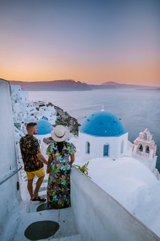 Santorini Greece, young couple on luxury vacation at the Island of Santorini watching sunrise by the blue dome church and whitewashed village of Oia Santorini Greece during sunrise during summer vacation, men and woman on holiday in Greece