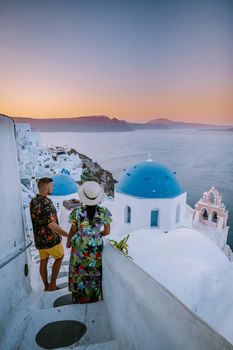 Santorini Greece, young couple on luxury vacation at the Island of Santorini watching sunrise by the blue dome church and whitewashed village of Oia Santorini Greece during sunrise during summer vacation, men and woman on holiday in Greece