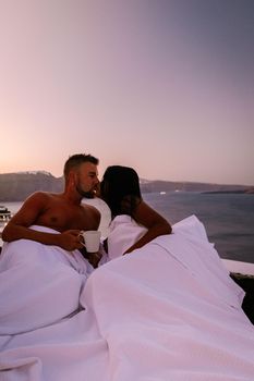 Santorini Greece, young couple on luxury vacation at the Island of Santorini watching sunrise by the blue dome church and whitewashed village of Oia Santorini Greece during sunrise during summer vacation, men and woman on holiday in Greece