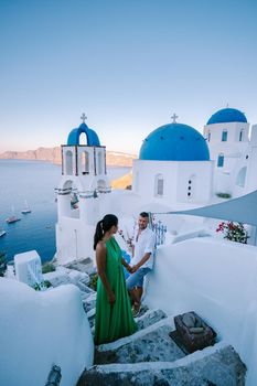 Santorini Greece, young couple on luxury vacation at the Island of Santorini watching sunrise by the blue dome church and whitewashed village of Oia Santorini Greece during sunrise during summer vacation, men and woman on holiday in Greece