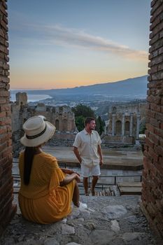 couple men and woman visit Ruins of Ancient Greek theatre in Taormina on background of Etna Volcano, Italy. Taormina located in Metropolitan City of Messina, on east coast of island of Sicily Italy