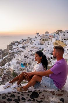 Santorini Greece, young couple on luxury vacation at the Island of Santorini watching sunrise by the blue dome church and whitewashed village of Oia Santorini Greece during sunrise during summer vacation, men and woman on holiday in Greece