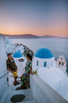 Santorini Greece, young couple on luxury vacation at the Island of Santorini watching sunrise by the blue dome church and whitewashed village of Oia Santorini Greece during sunrise during summer vacation, men and woman on holiday in Greece