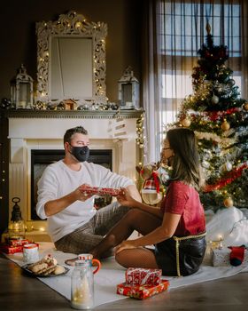 Christmas couple wearing mask during Christmas night,Close up portrait of happy mixed-races couple with christmas presents and wearing medical masks in quarantine. couple with face mask during covid outbreak pandemic