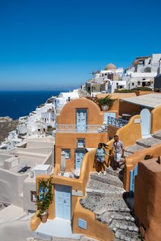 Santorini Greece, young couple on luxury vacation at the Island of Santorini watching sunrise by the blue dome church and whitewashed village of Oia Santorini Greece during sunrise during summer vacation, men and woman on holiday in Greece