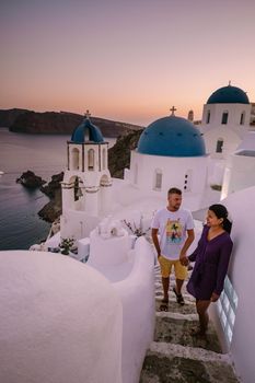 Santorini Greece, young couple on luxury vacation at the Island of Santorini watching sunrise by the blue dome church and whitewashed village of Oia Santorini Greece during sunrise during summer vacation