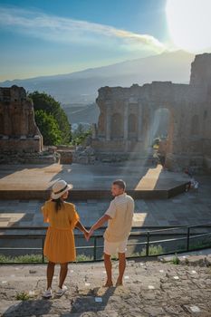 couple men and woman visit Ruins of Ancient Greek theatre in Taormina on background of Etna Volcano, Italy. Taormina located in Metropolitan City of Messina, on east coast of island of Sicily Italy