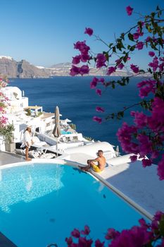 Couple at luxury infinity pool,Santorini Greece, young couple on luxury vacation at the Island of Santorini watching sunrise by the blue dome church and whitewashed village of Oia Santorini Greece . Europe