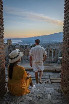 couple men and woman visit Ruins of Ancient Greek theatre in Taormina on background of Etna Volcano, Italy. Taormina located in Metropolitan City of Messina, on east coast of island of Sicily Italy