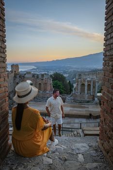 couple men and woman visit Ruins of Ancient Greek theatre in Taormina on background of Etna Volcano, Italy. Taormina located in Metropolitan City of Messina, on east coast of island of Sicily Italy