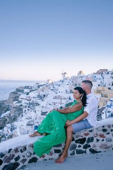 Santorini Greece, young couple on luxury vacation at the Island of Santorini watching sunrise by the blue dome church and whitewashed village of Oia Santorini Greece during sunrise during summer vacation, men and woman on holiday in Greece