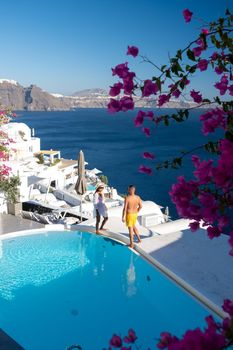 Couple at luxury infinity pool,Santorini Greece, young couple on luxury vacation at the Island of Santorini watching sunrise by the blue dome church and whitewashed village of Oia Santorini Greece . Europe