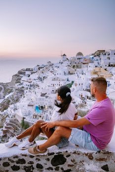 Santorini Greece, young couple on luxury vacation at the Island of Santorini watching sunrise by the blue dome church and whitewashed village of Oia Santorini Greece . Europe