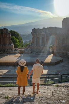 couple men and woman visit Ruins of Ancient Greek theatre in Taormina on background of Etna Volcano, Italy. Taormina located in Metropolitan City of Messina, on east coast of island of Sicily Italy