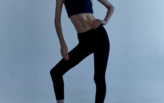 A sportive woman in leggings and a T-shirt is engaged in fitness on a light background. High quality photo