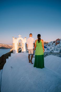 Santorini Greece, young couple on luxury vacation at the Island of Santorini watching sunrise by the blue dome church and whitewashed village of Oia Santorini Greece during sunrise during summer vacation, men and woman on holiday in Greece