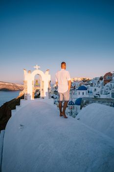 Sunset at the Island Of Santorini Greece, beautiful whitewashed village Oia with church and windmill during sunset, streets of Oia Santorini during summer vacation at the Greek Island, young men on luxury vacation Santorini