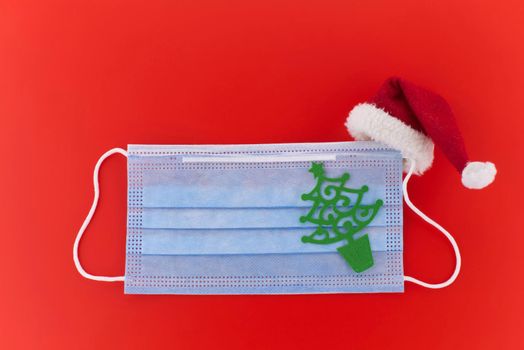Face mask with paper cut Christmas tree and and Santa hat over a red background with copyspace