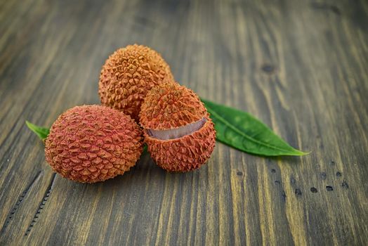 Lychee fruit whole and opened with green leaves decoration on rustic wood background