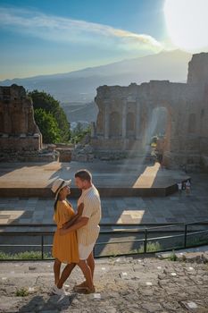 couple men and woman visit Ruins of Ancient Greek theatre in Taormina on background of Etna Volcano, Italy. Taormina located in Metropolitan City of Messina, on east coast of island of Sicily Italy