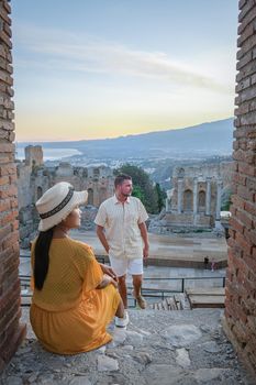 couple men and woman visit Ruins of Ancient Greek theatre in Taormina on background of Etna Volcano, Italy. Taormina located in Metropolitan City of Messina, on east coast of island of Sicily Italy