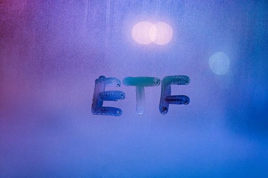abbreviation word etf - exchange traded funds - handwritten on foggy glass window at night with neon blue back street lights