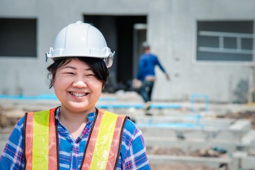 Asian woman civil construction engineer worker or architect with helmet and safety vest happy working at a building or construction site