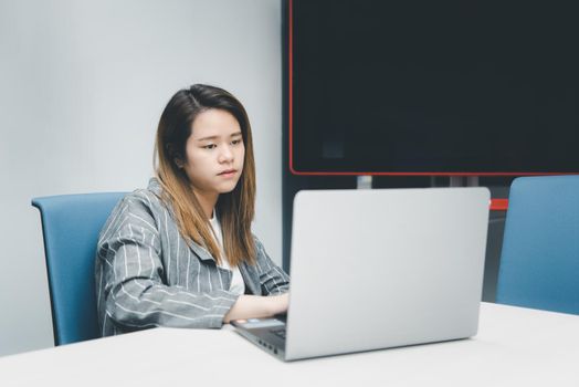 Asian woman is student,businesswoman working by computer notebook, laptop in office meeting room with whiteboard background with annoyed, displeased emotion in concept working woman,unhappy in life