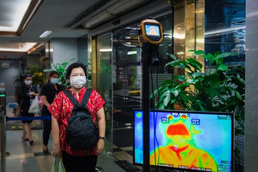 Asian people waiting for body temperature check before access to building for against epidemic flu covid19 or corona virus influenza in office by thermoscan or infrared thermal camera