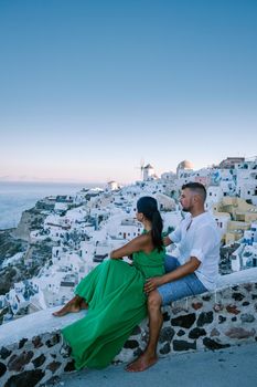 Santorini Greece, young couple on luxury vacation at the Island of Santorini watching sunrise by the blue dome church and whitewashed village of Oia Santorini Greece during sunrise during summer vacation, men and woman on holiday in Greece