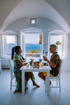 breakfast at traditional historical cave house Santorini Greece, young couple on luxury vacation at the Island of Santorini watching sunrise by the blue dome church and whitewashed village of Oia Santorini Greece during sunrise during summer vacation, 