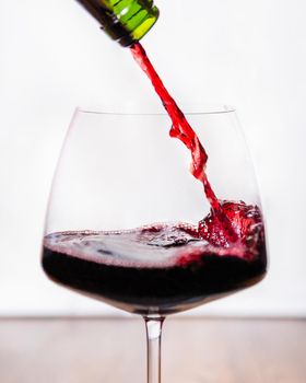 Red wine pouring to the glass, white background