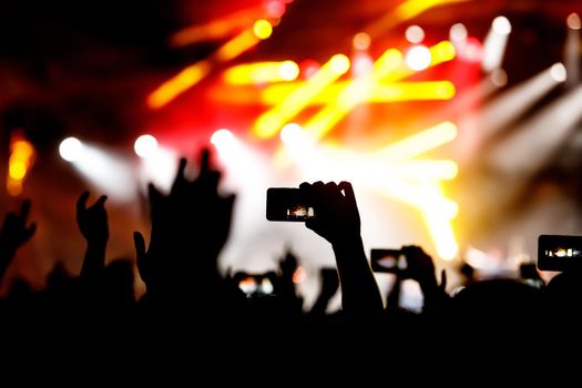 Hands and smartphones in front of the stage. Crowd at a concert.