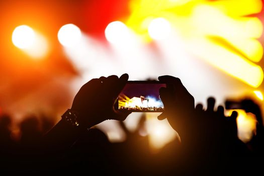 Hands and smartphones in front of the stage. Crowd at a concert.