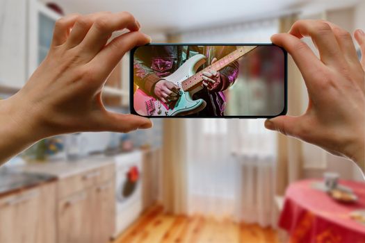 Watching online music concert at home using a mobile phone. Guitar close-up on the screen