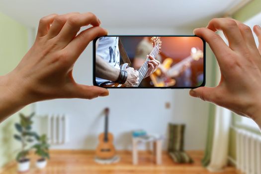 Watching online music concert at home using a mobile phone. Guitar close-up on the screen