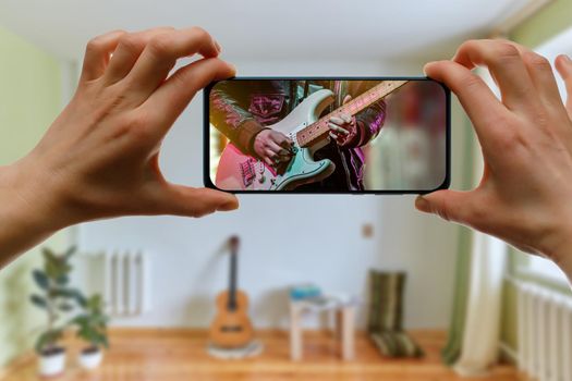 Online music lesson via mobile phone at home. Guitar teacher hands on screen.