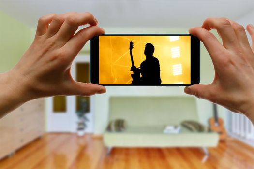 Watching online music concert at home using a mobile phone. Guitar close-up on the screen