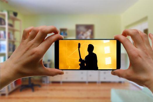 Watching online music concert at home using a mobile phone. Guitar close-up on the screen