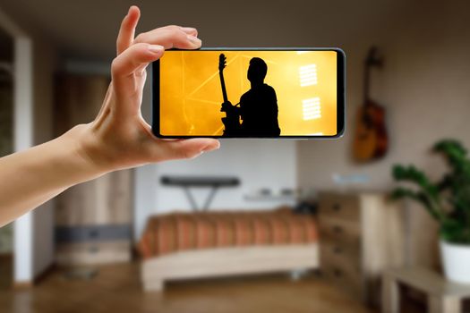 Watching online music concert at home using a mobile phone. Guitar close-up on the screen