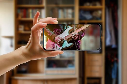 Watching online music concert at home using a mobile phone. Guitar close-up on the screen