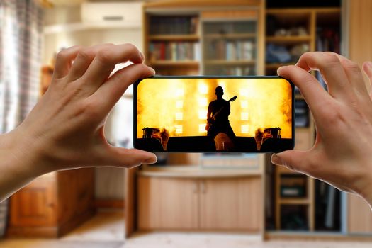 Watching online music concert at home using a mobile phone. Guitarist silhouette on the screen