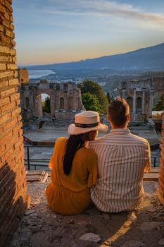 couple men and woman visit Ruins of Ancient Greek theatre in Taormina on background of Etna Volcano, Italy. Taormina located in Metropolitan City of Messina, on east coast of island of Sicily Italy