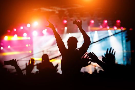 Silhouettes of people with raised hands at a concert. Stage light