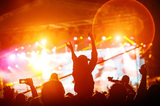 The crowd with their hands up enjoys music concert. Fan silhouette on stage background